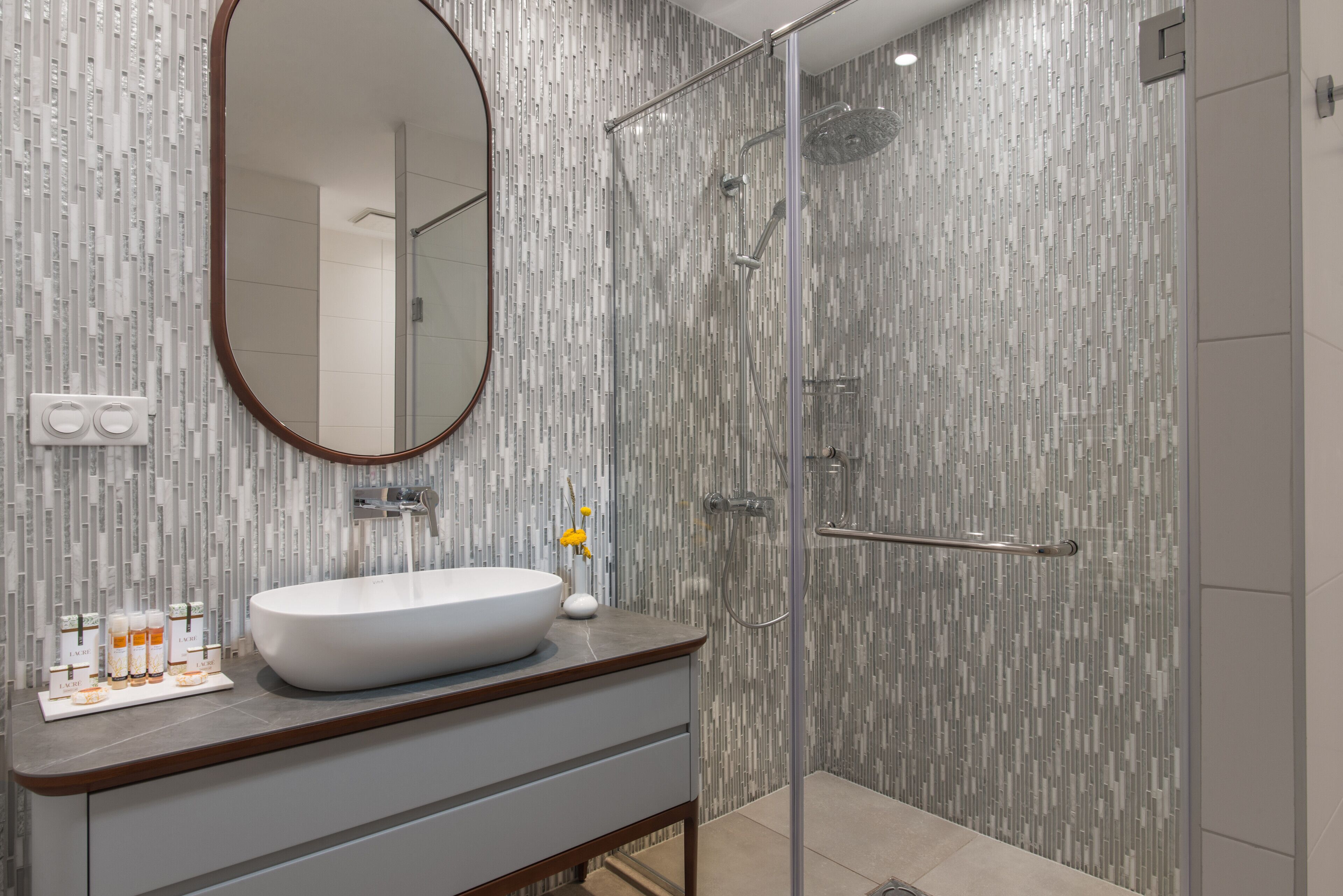 A modern bathroom with a large oval sink, a glass shower enclosure, and a mirror with a wooden frame.