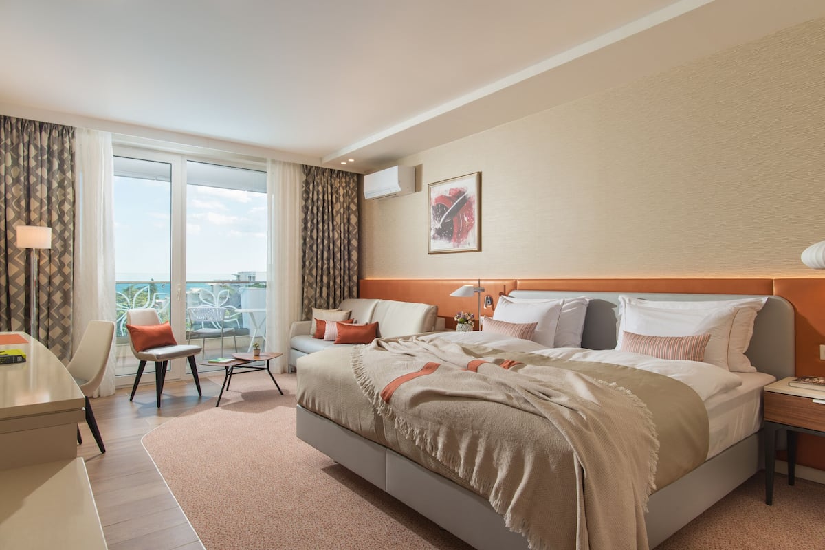Una habitación de hotel moderna con una cama grande, un escritorio, una silla y un balcón con vistas.