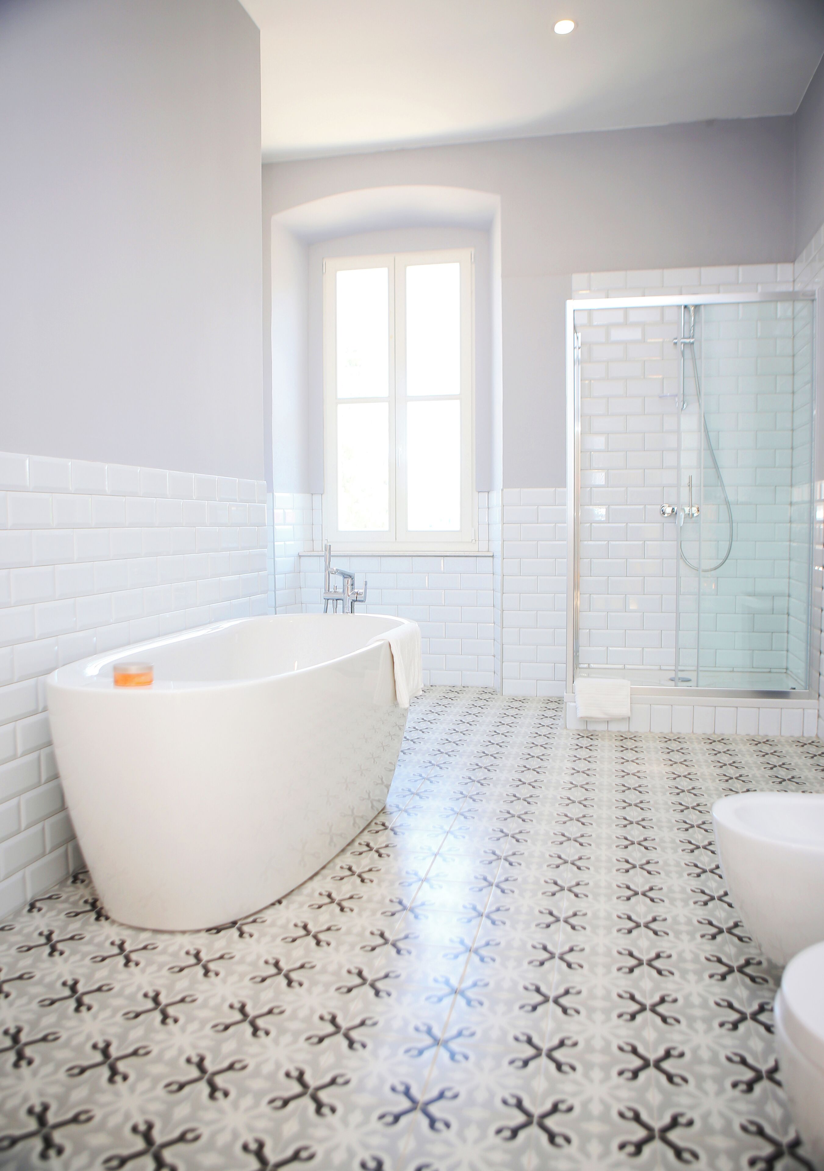 A bathroom with a freestanding bathtub, a glass-enclosed shower, and a patterned floor.