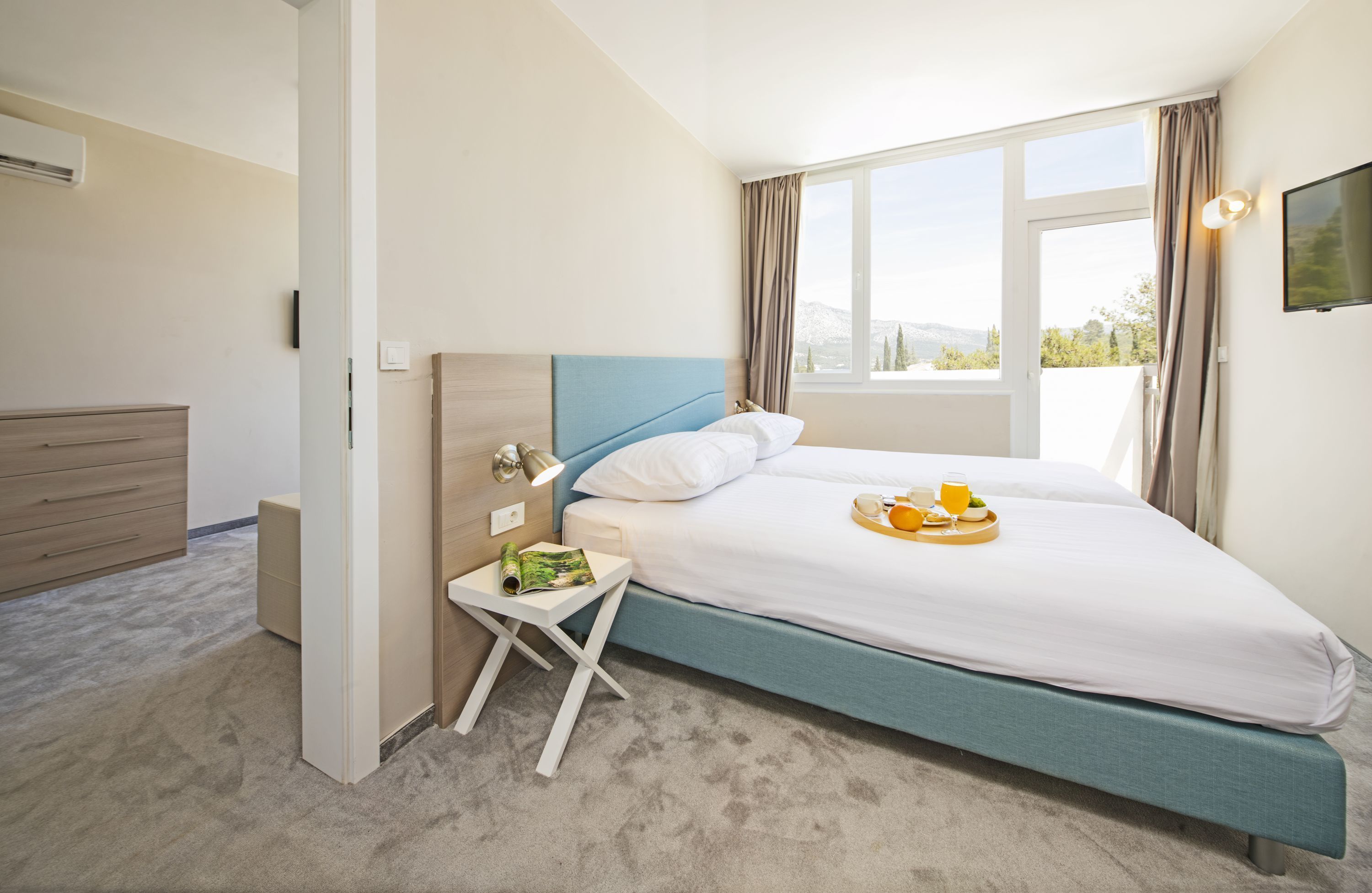 Ett modernt hotellrum med en stor säng, ett litet sidobord, en TV och ett fönster med gardiner.