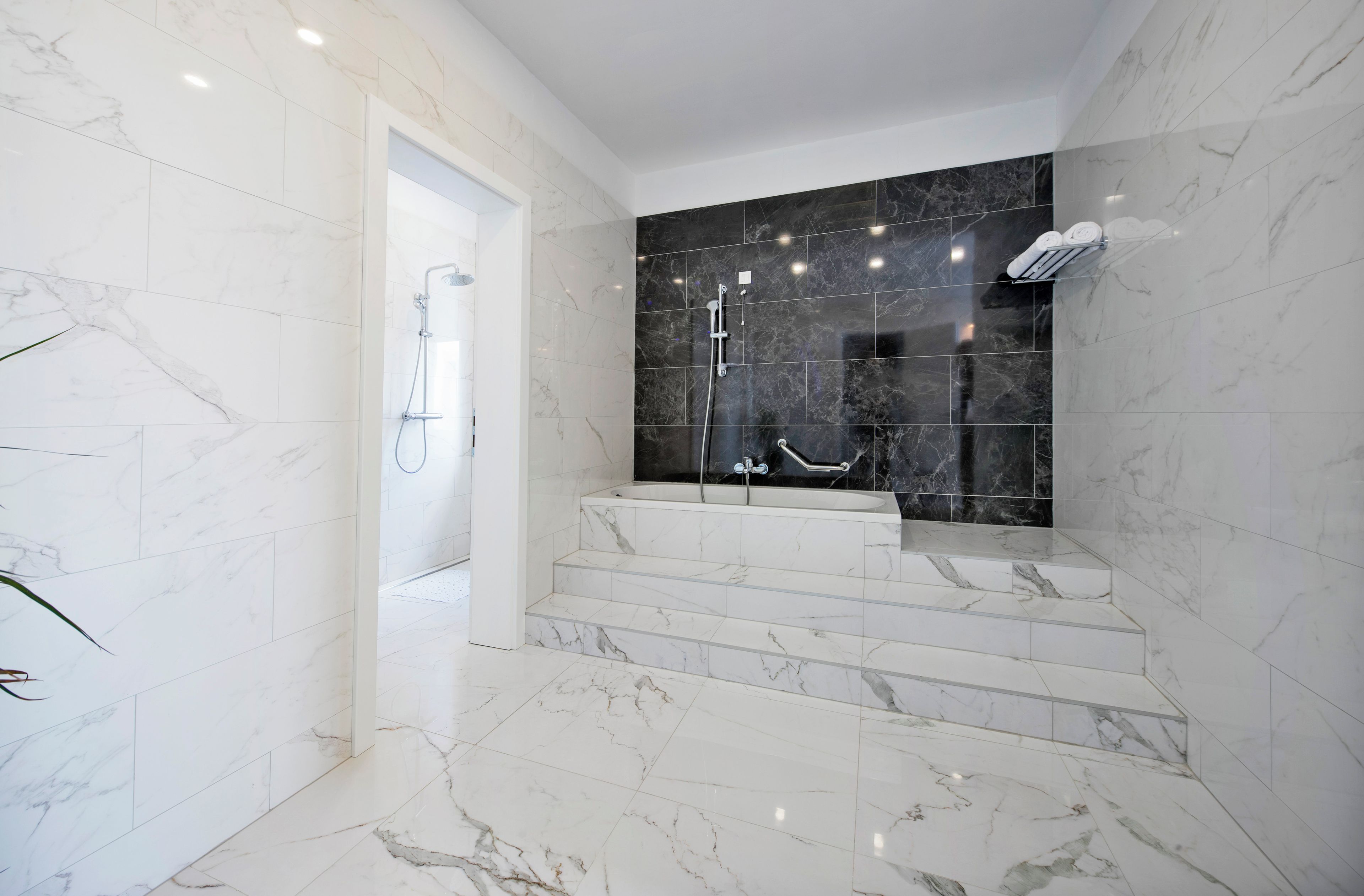 A modern bathroom with a marble floor, a bathtub, and a shower area.