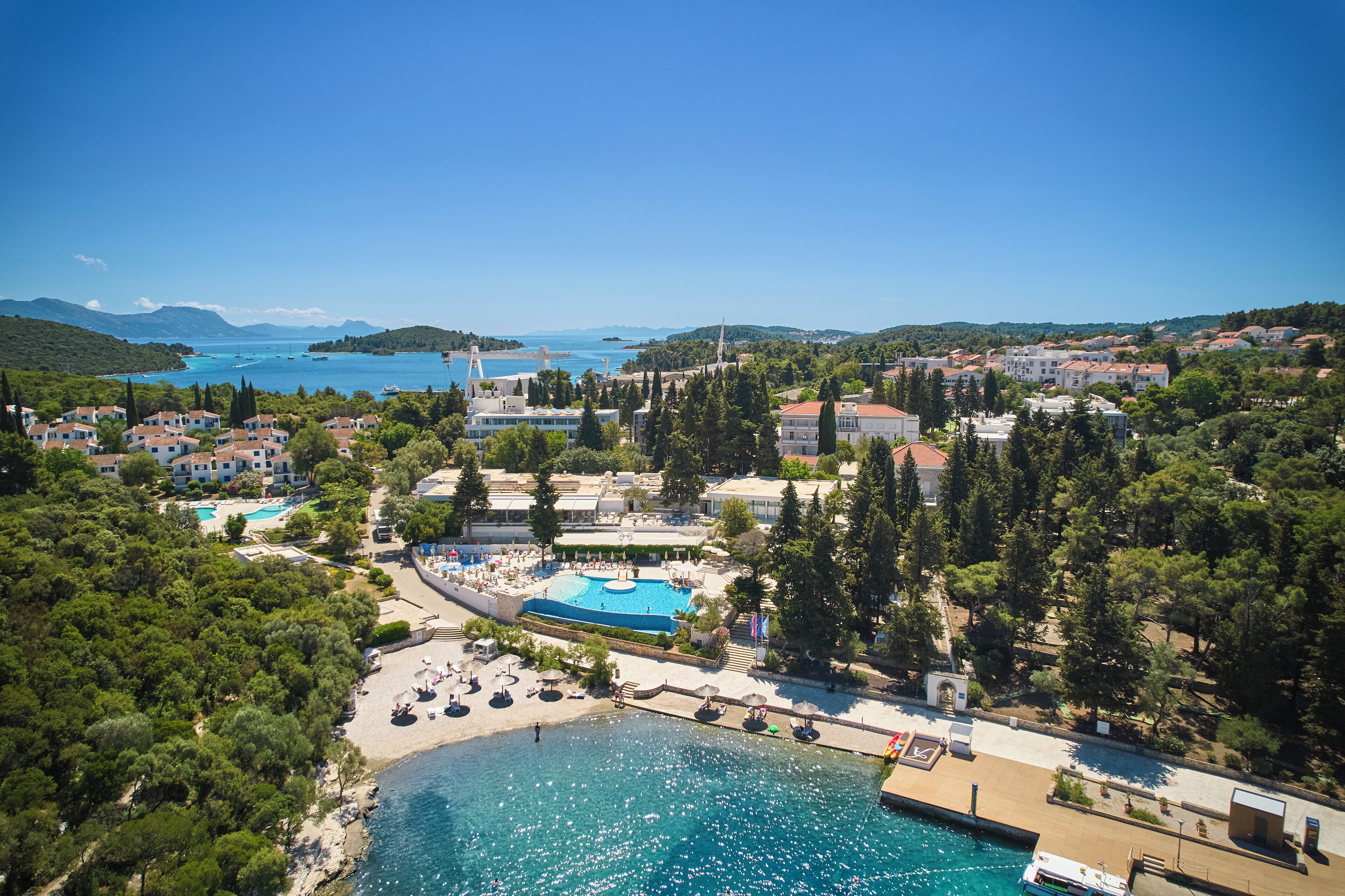 A coastal resort with a swimming pool, beach, and views of the sea and mountains.