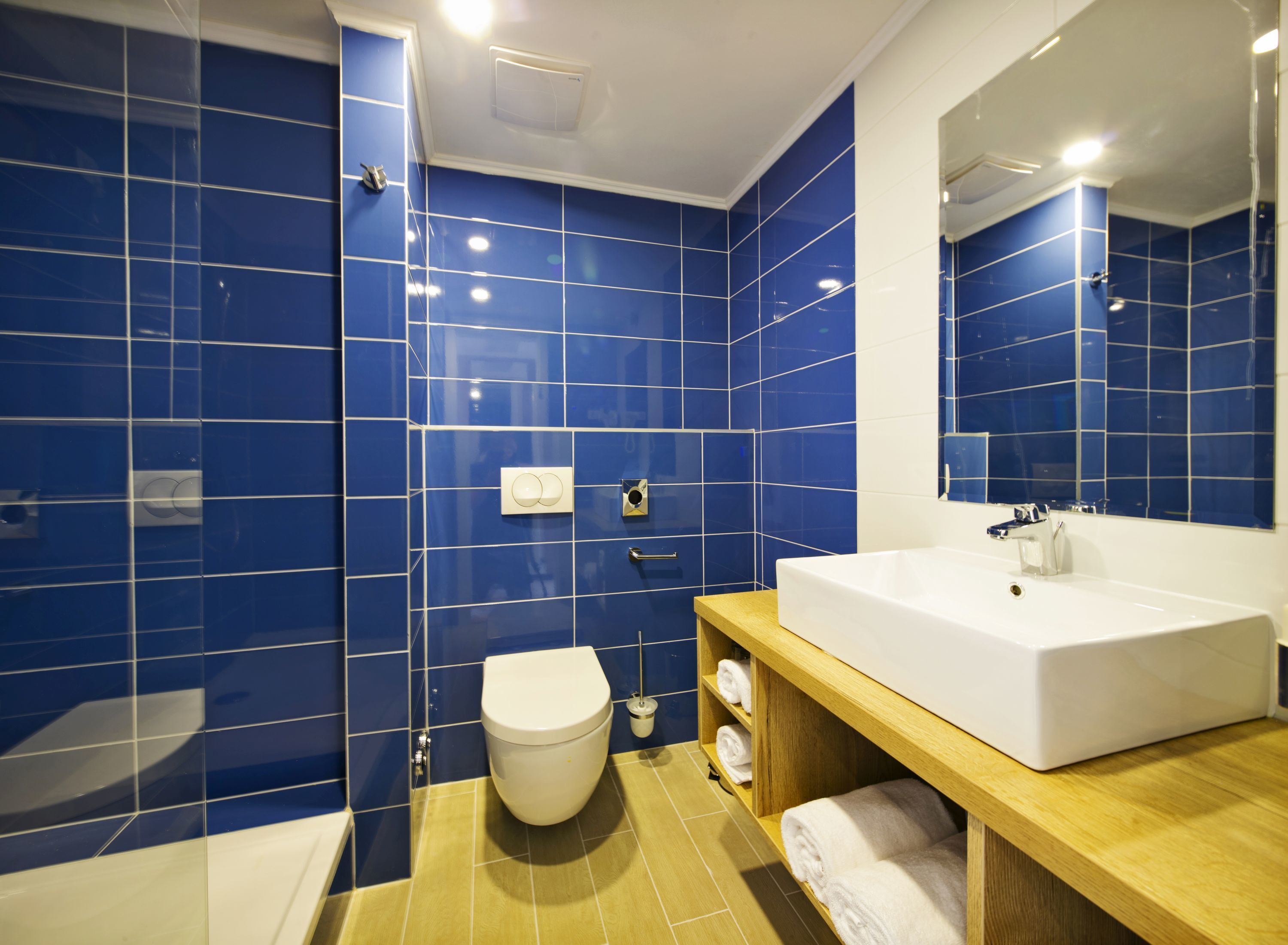 A modern bathroom with blue tiles, a white sink, and a wooden vanity.