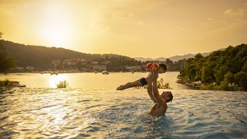 A man lifting a child in a swimming pool with a sunset in the background.