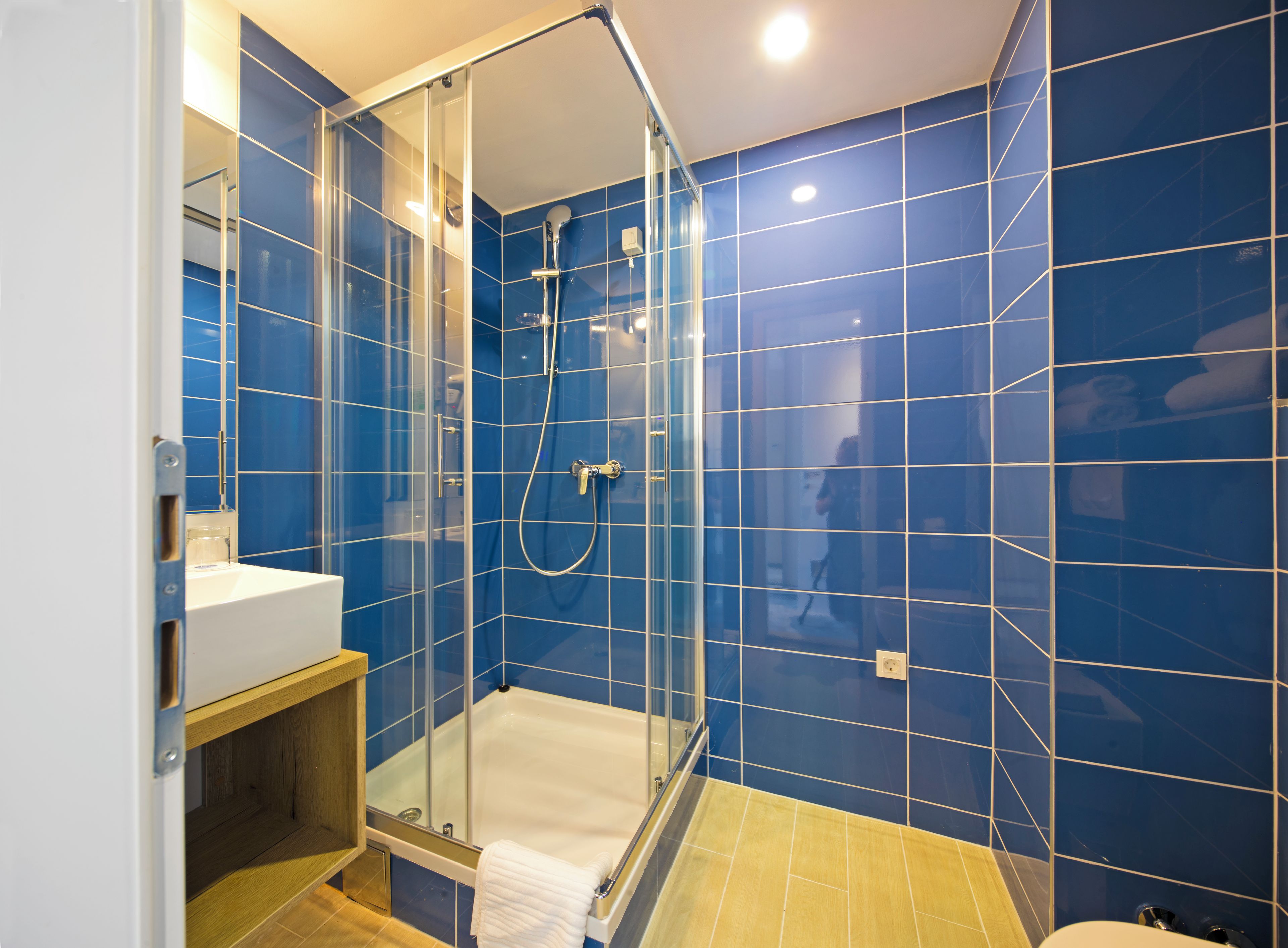 Een moderne badkamer met een douchecabine van glas, een witte wastafel en blauwe wandtegels.