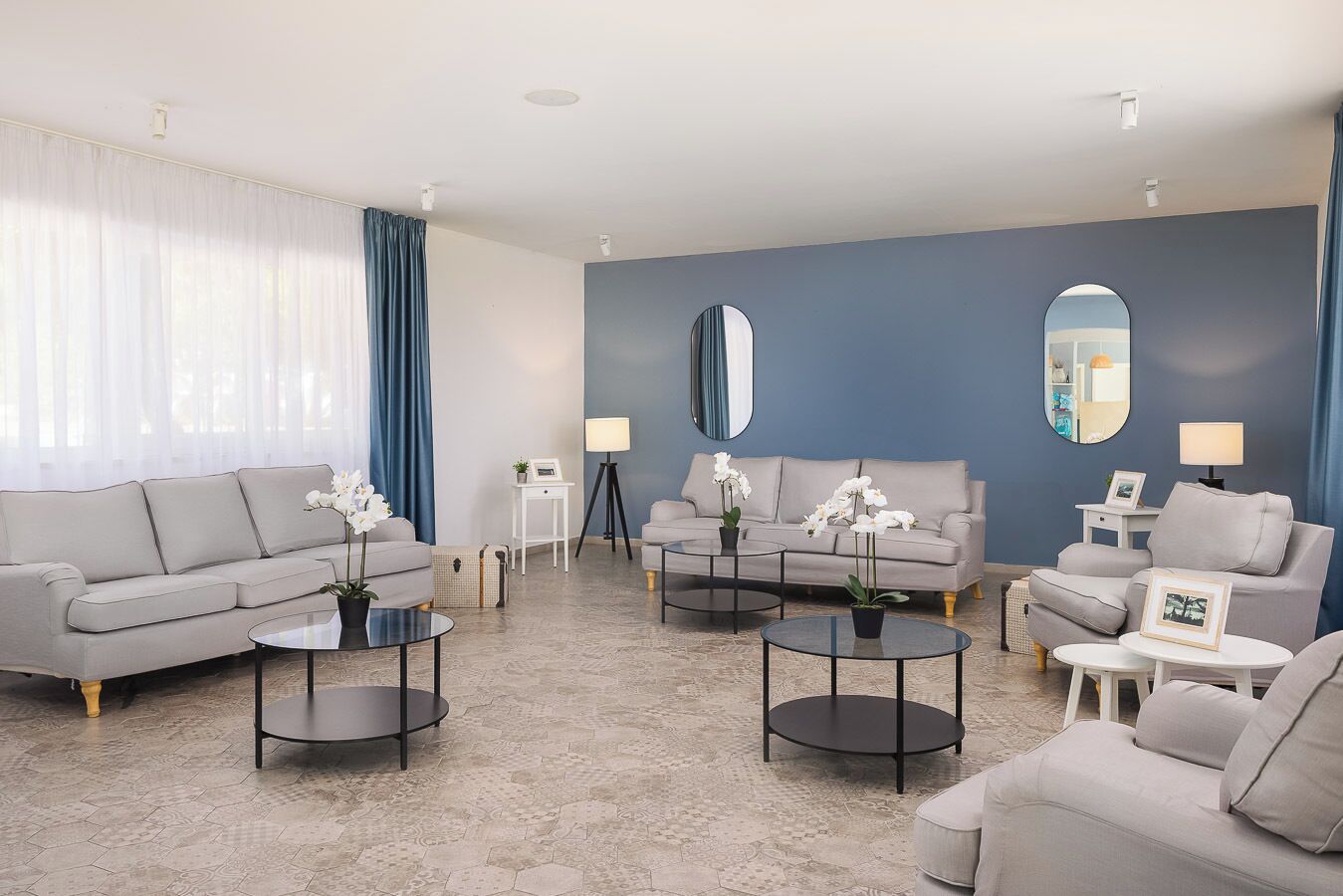 Ein modernes Wohnzimmer mit grauem Sofa, zwei Sesseln, einem Couchtisch und einer Stehlampe.