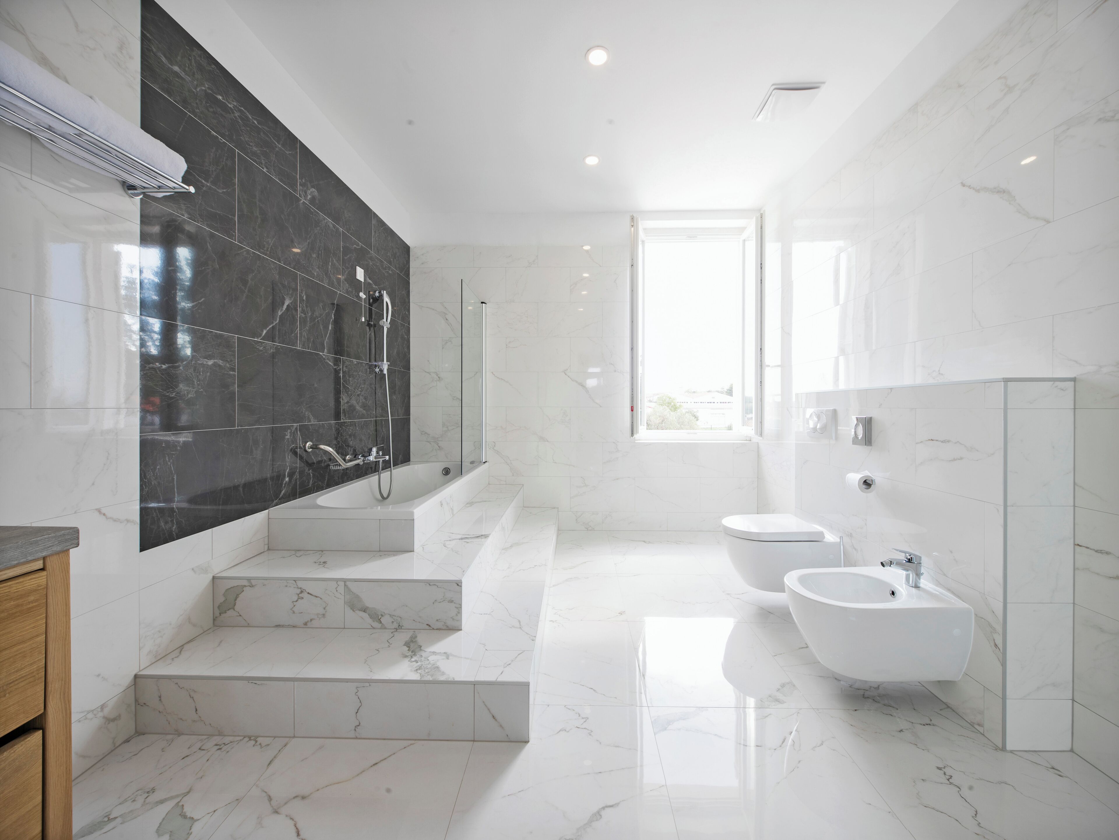 A modern bathroom with a large bathtub, two sinks, and a shower area.