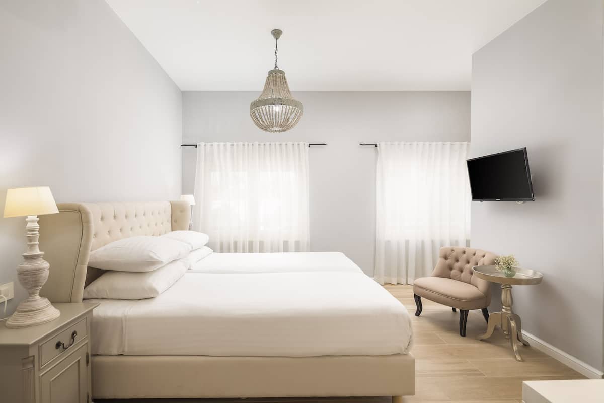 Quarto com cama, mesa de cabeceira, luminária, cadeira, televisão e cortinas.