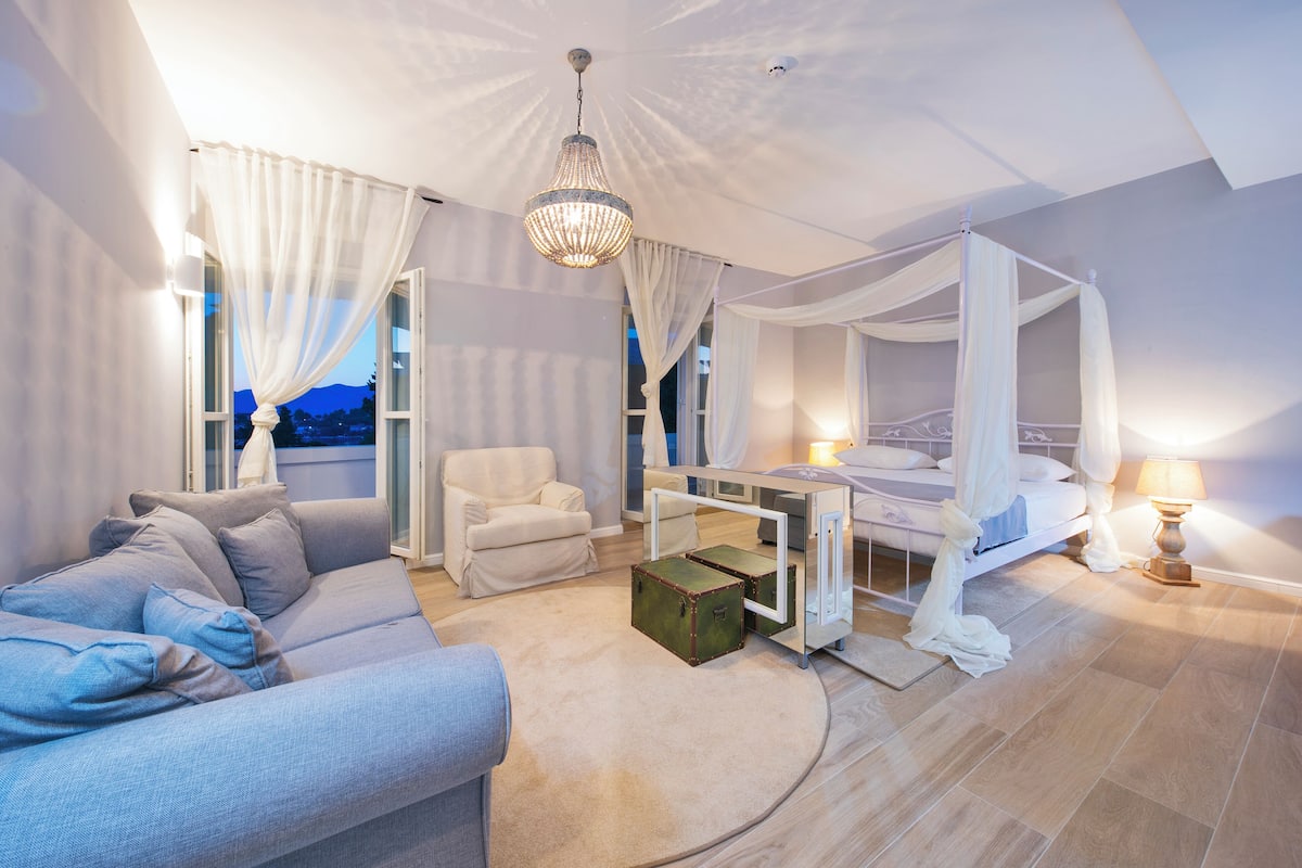 Quarto com cama de dossel, um espaço de estar com sofá e vista para as montanhas pela janela.