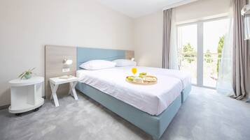 A hotel room with a bed, a bedside table, a small table with a plant, and a window with curtains.