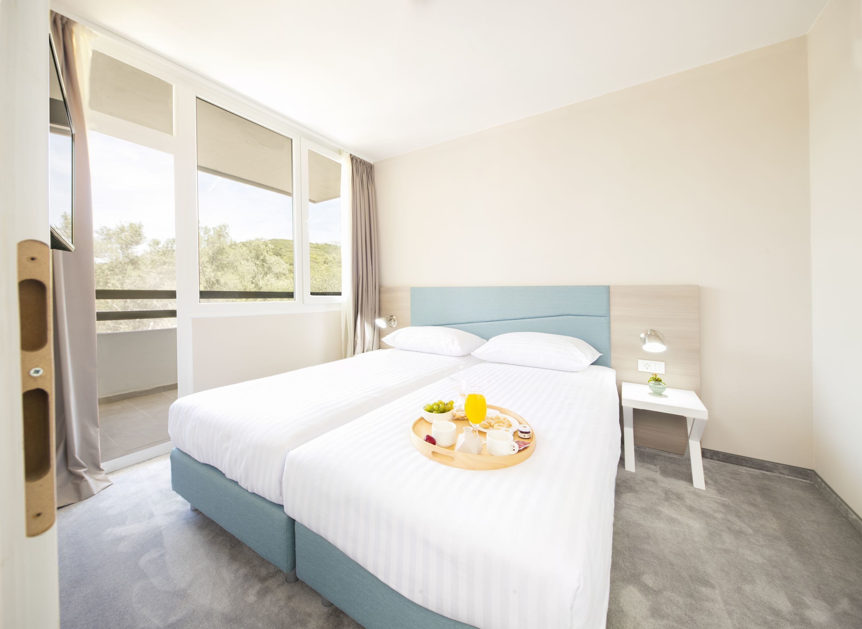 Camera d'albergo con un letto grande, un comodino con una lampada e un vassoio con prodotti per la colazione.