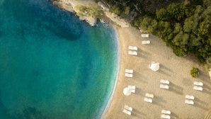 An aerial view of a beach with clear turquoise waters, sandy shore, and white lounge chairs arranged along the beach.