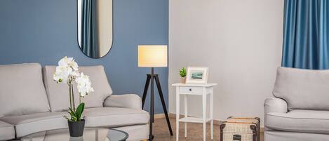 A modern living room with a sofa, a glass coffee table, a lamp, a small side table, and a wicker basket.