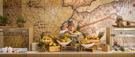 A buffet setup with various fruits and a chef in the background.