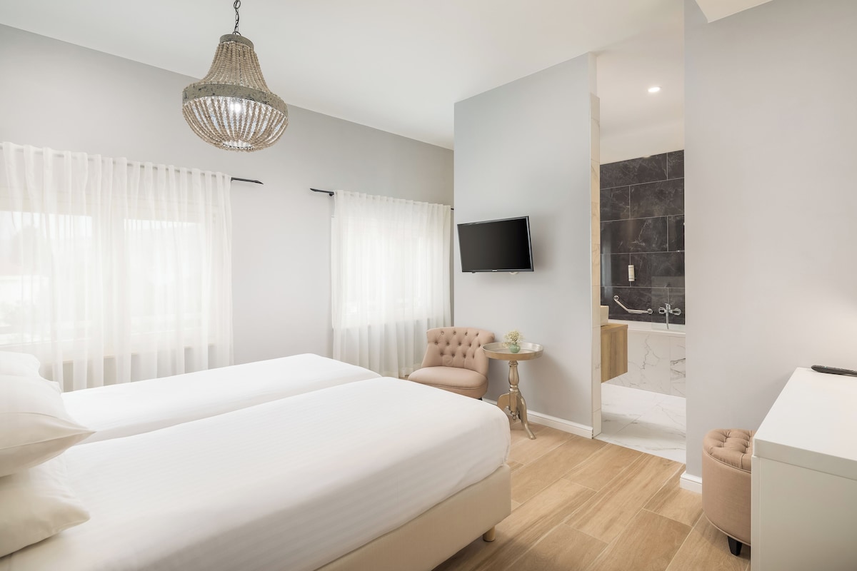 A modern hotel room with a large bed, a television, a small table, and a bathroom visible through an open door.