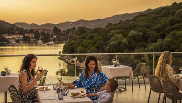 A dining table with plates, glasses, and cutlery, set against a backdrop of a lake and mountains.