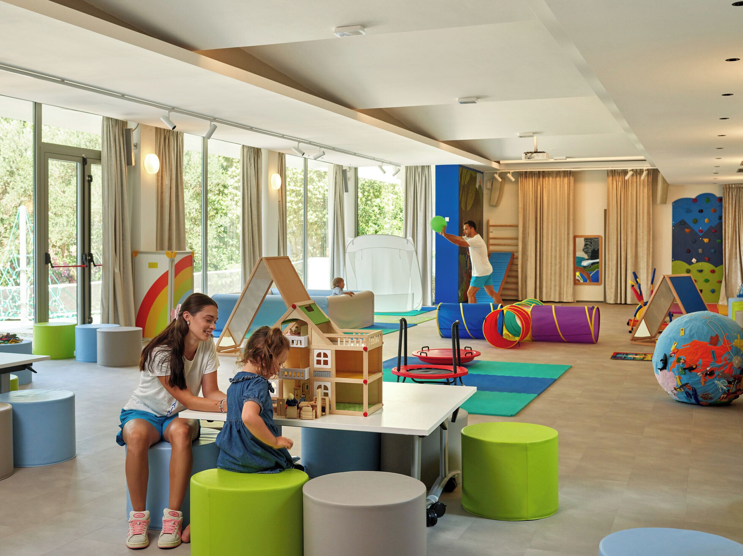 Un grand espace de jeux intérieur, doté de larges fenêtres, de structures colorées et de divers types de sièges.