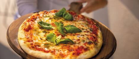 Pizza sobre una tabla de madera con ingredientes visibles y una persona al fondo.
