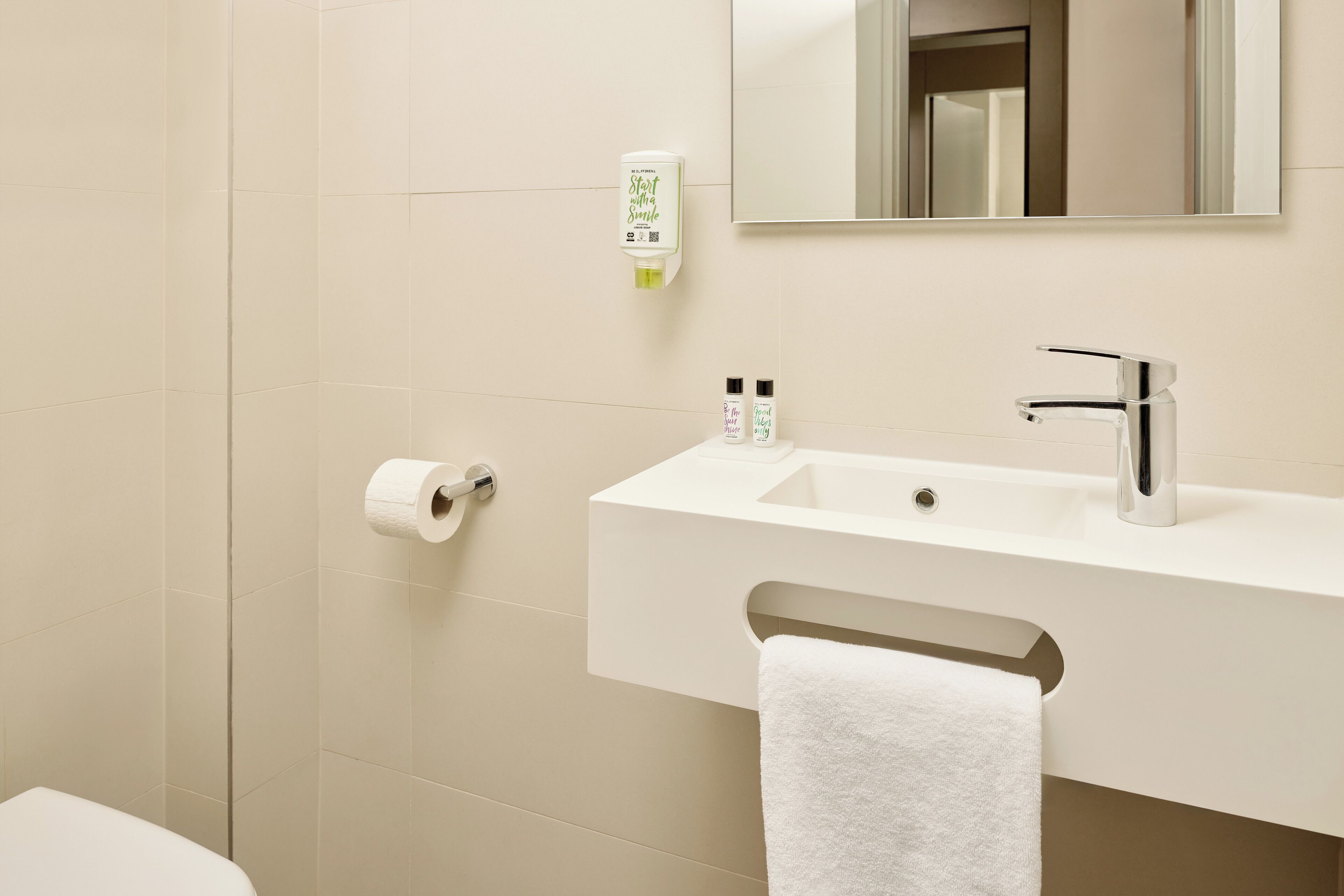 A bathroom with a white sink, a mirror, a towel rack, and a toilet paper holder.