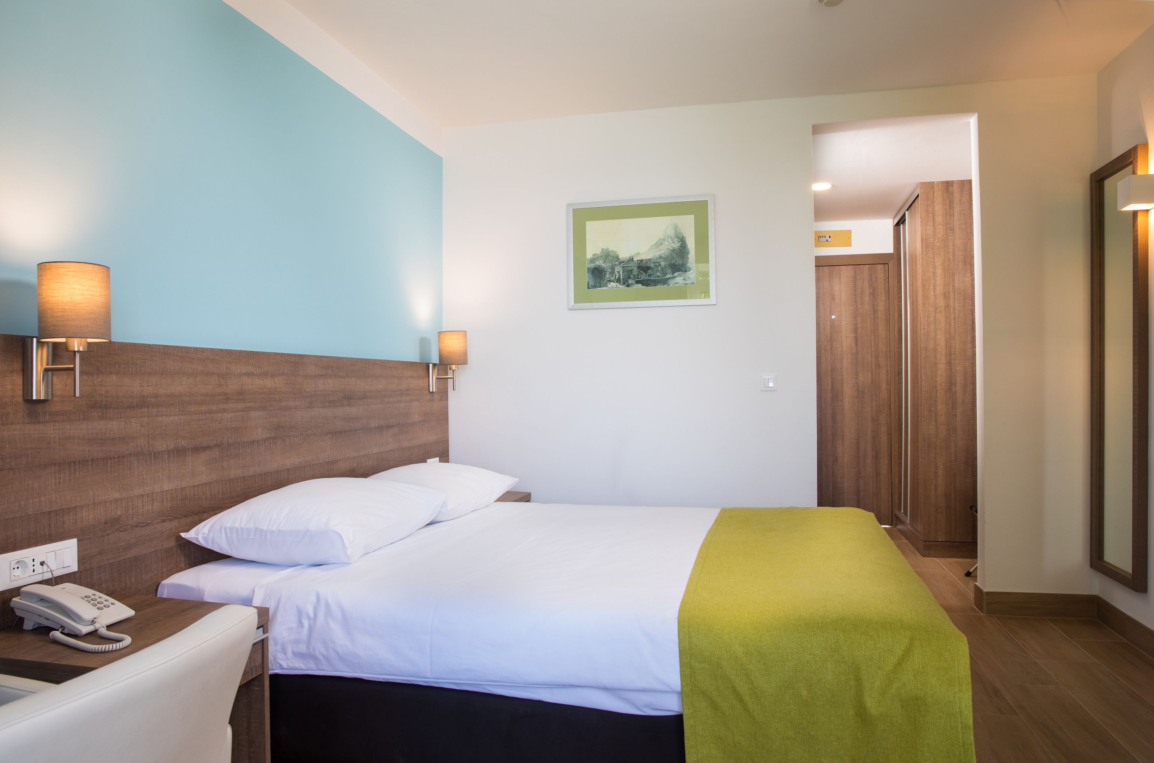 A hotel room with a bed, bedside lamps, a phone, and a painting on the wall.
