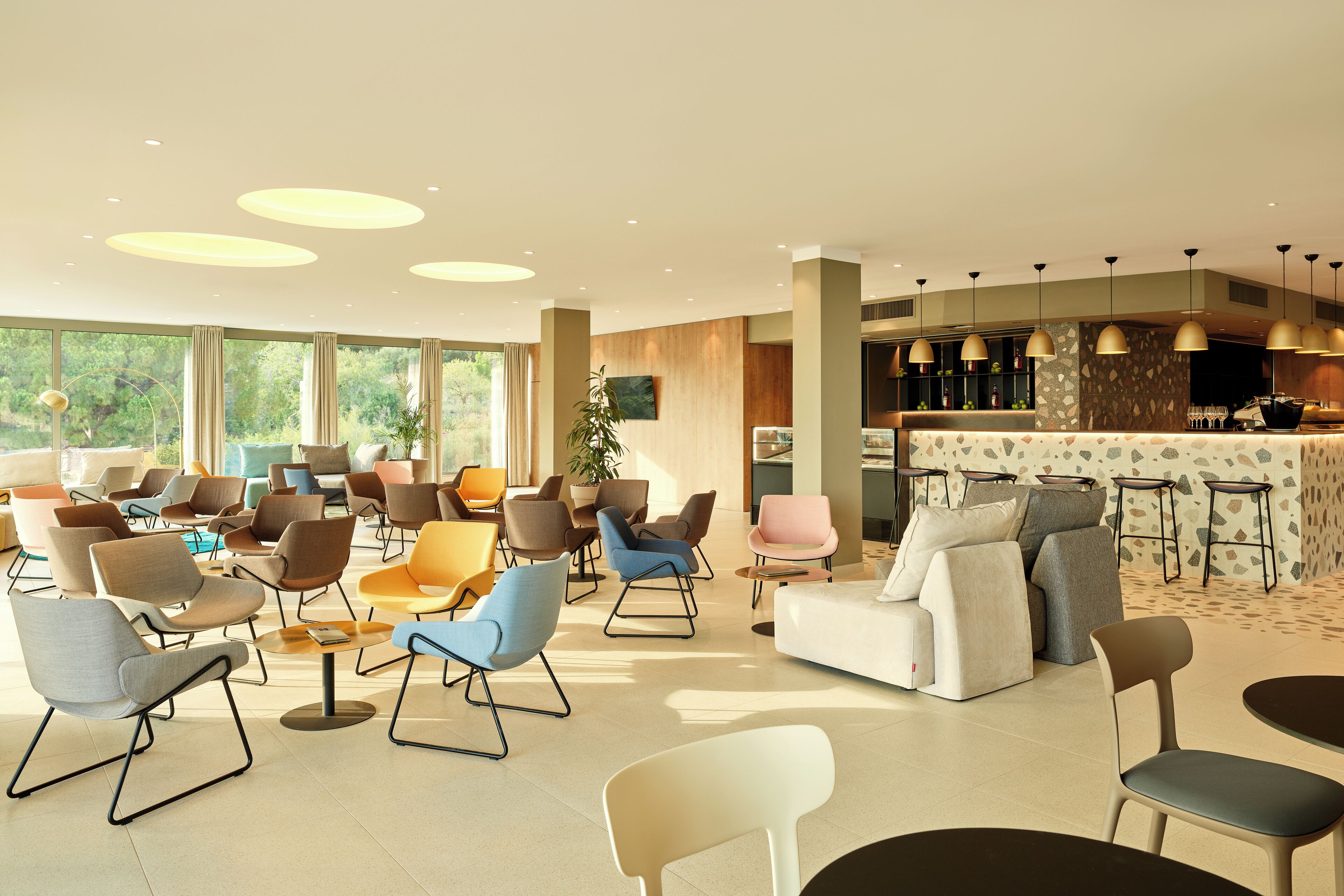 Un hall d’hôtel moderne doté de différents types de sièges, d’un bar et de grandes fenêtres offrant une vue sur l’extérieur.