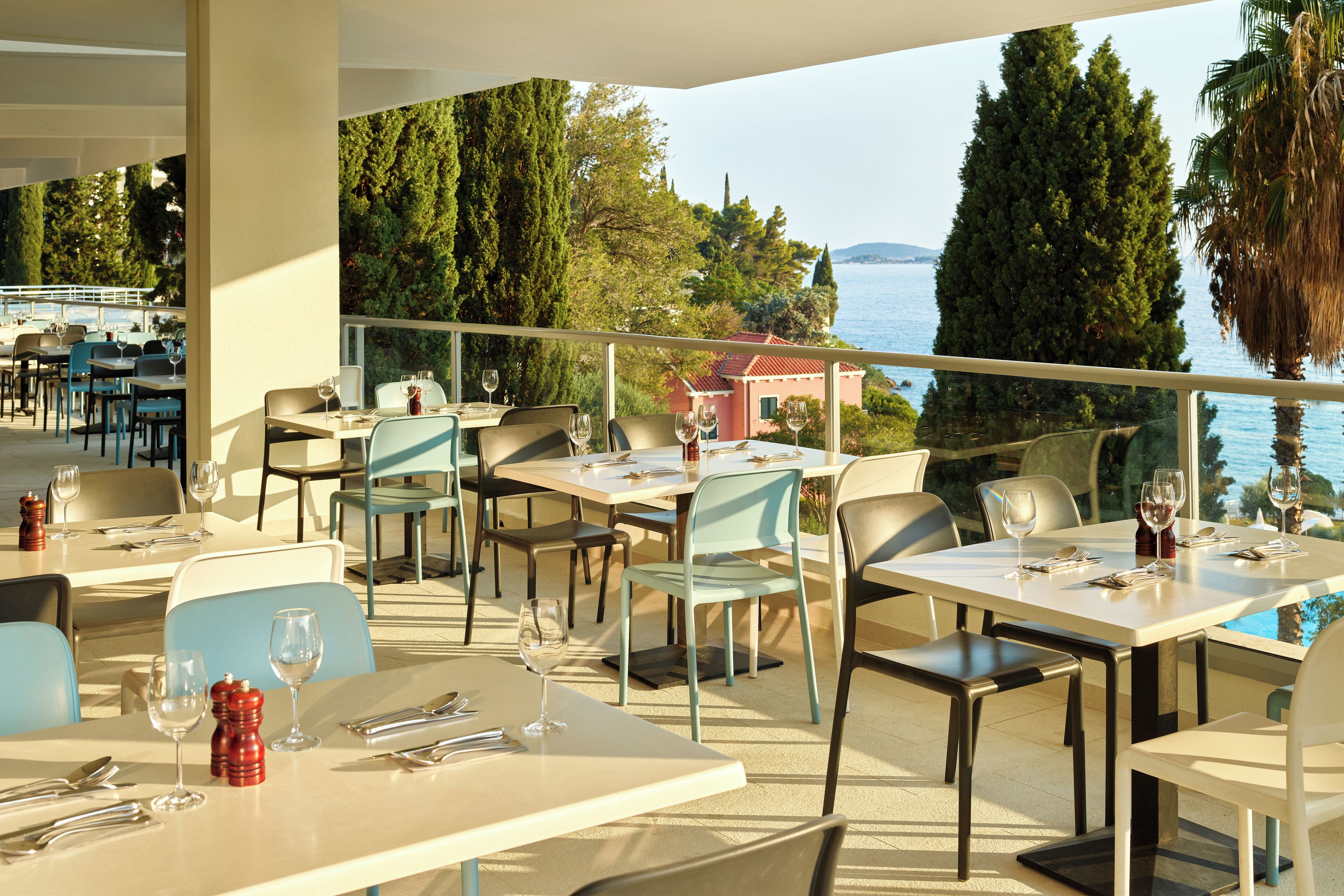 A restaurant with outdoor seating overlooking a body of water, featuring tables and chairs arranged for dining.