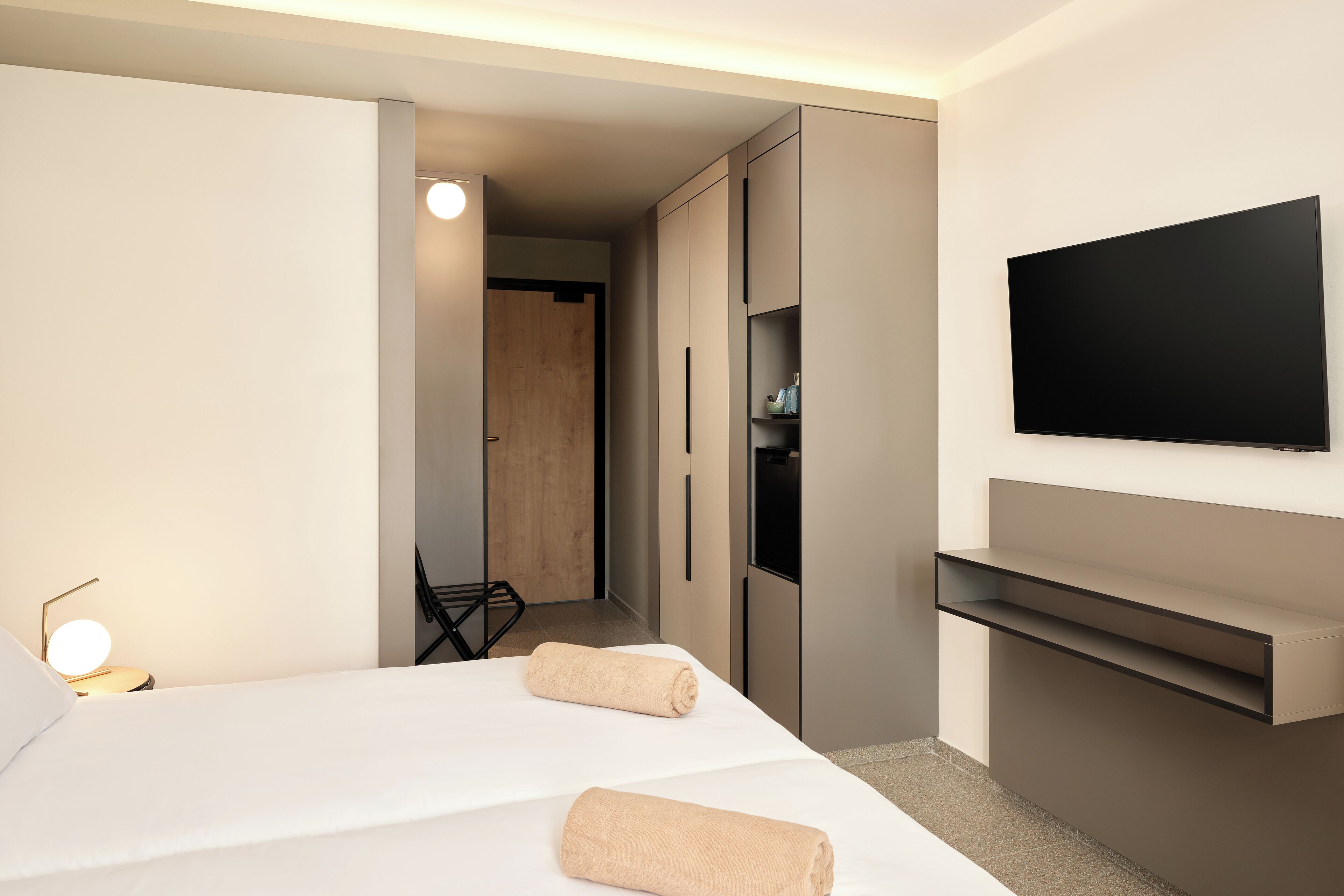 Une chambre d’hôtel moderne équipée d’un lit, d’un téléviseur fixé au mur et d’une armoire intégrée.