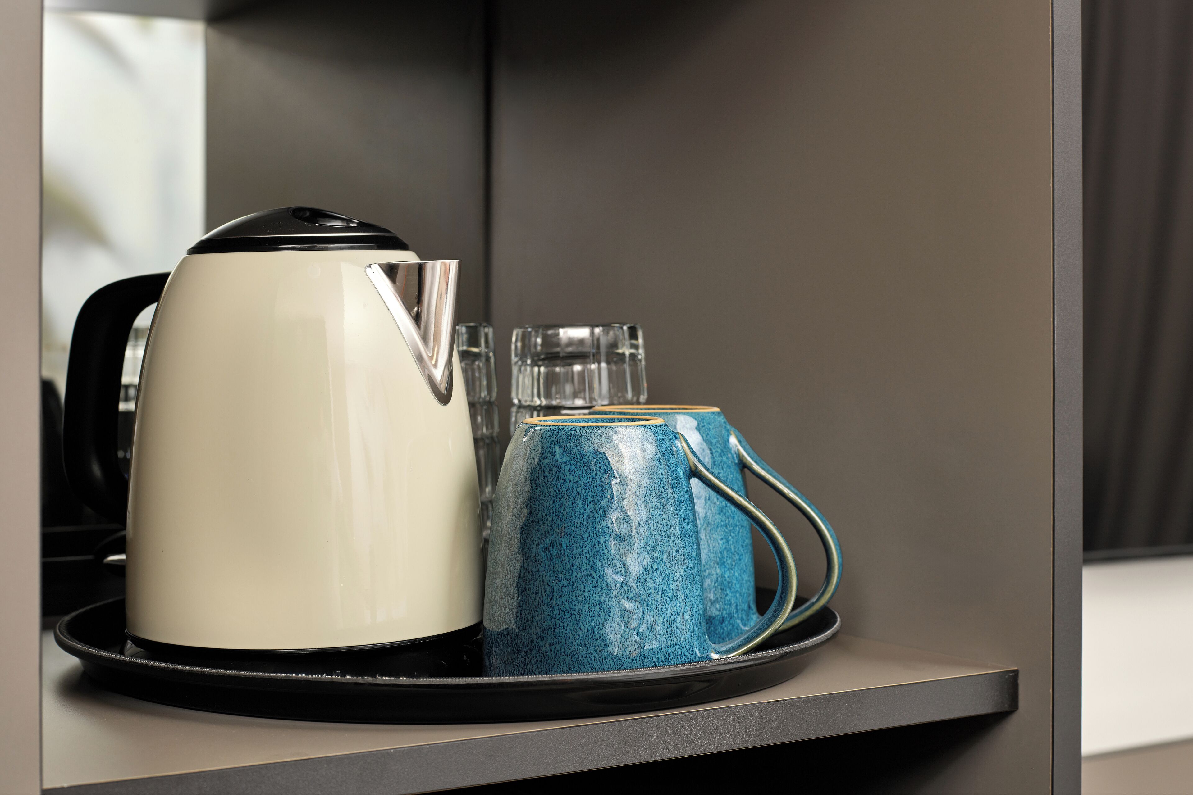 A white kettle and a blue mug on a tray.