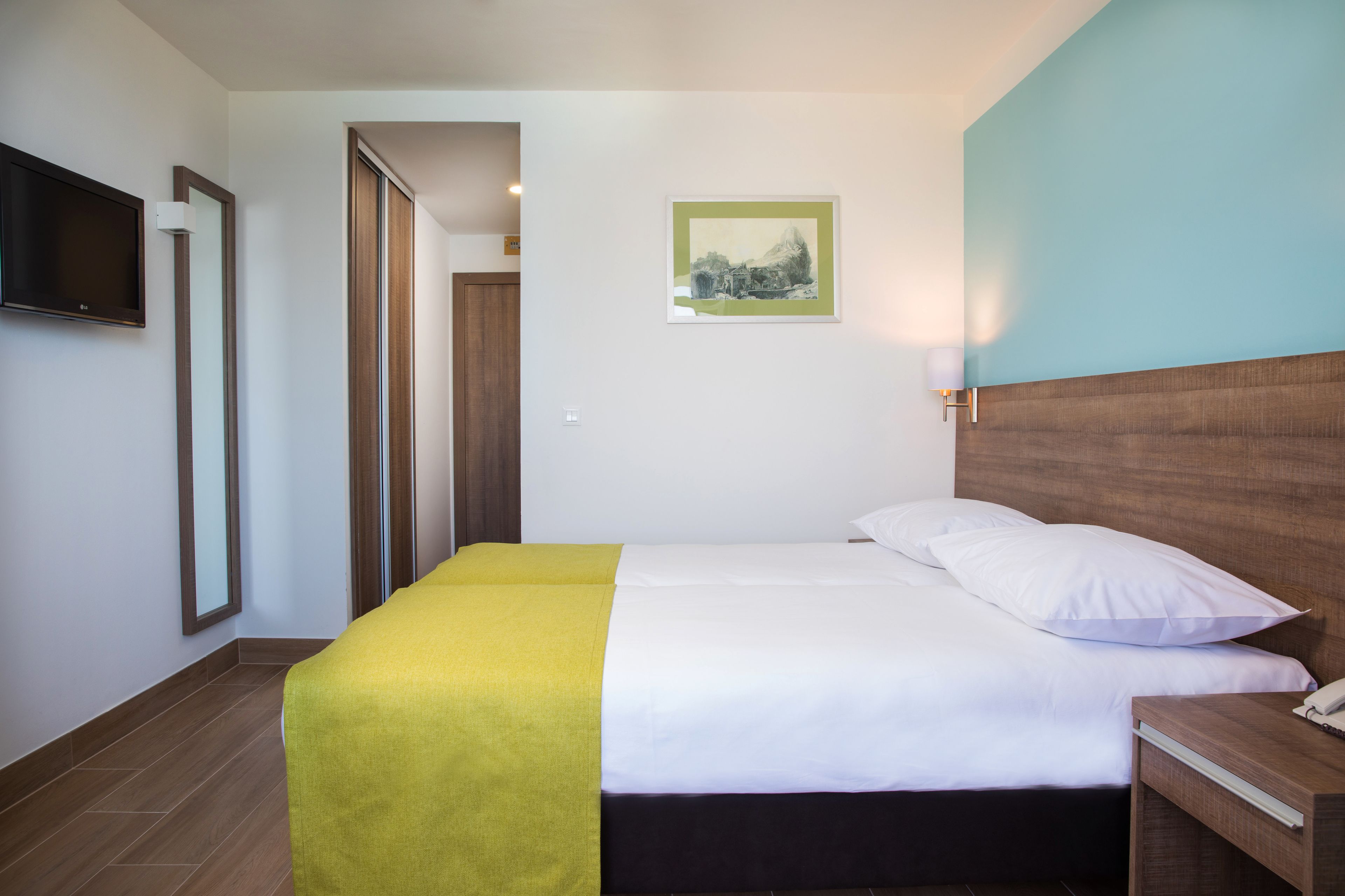 A hotel room with a bed, a bedside table, a TV mounted on the wall, and a framed picture on the wall.