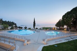 A pool area with two pools, lounge chairs, and a view of the sea at dusk. - Maistra Select Astarea Hotel (Zupa dubrovacka)