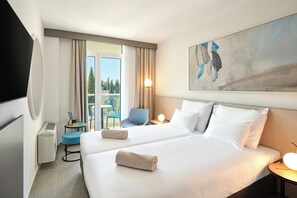 A hotel room with two beds, a TV, a desk with a lamp, a chair, and a view of trees through the window. - Maistra Select Astarea Hotel (Zupa dubrovacka)