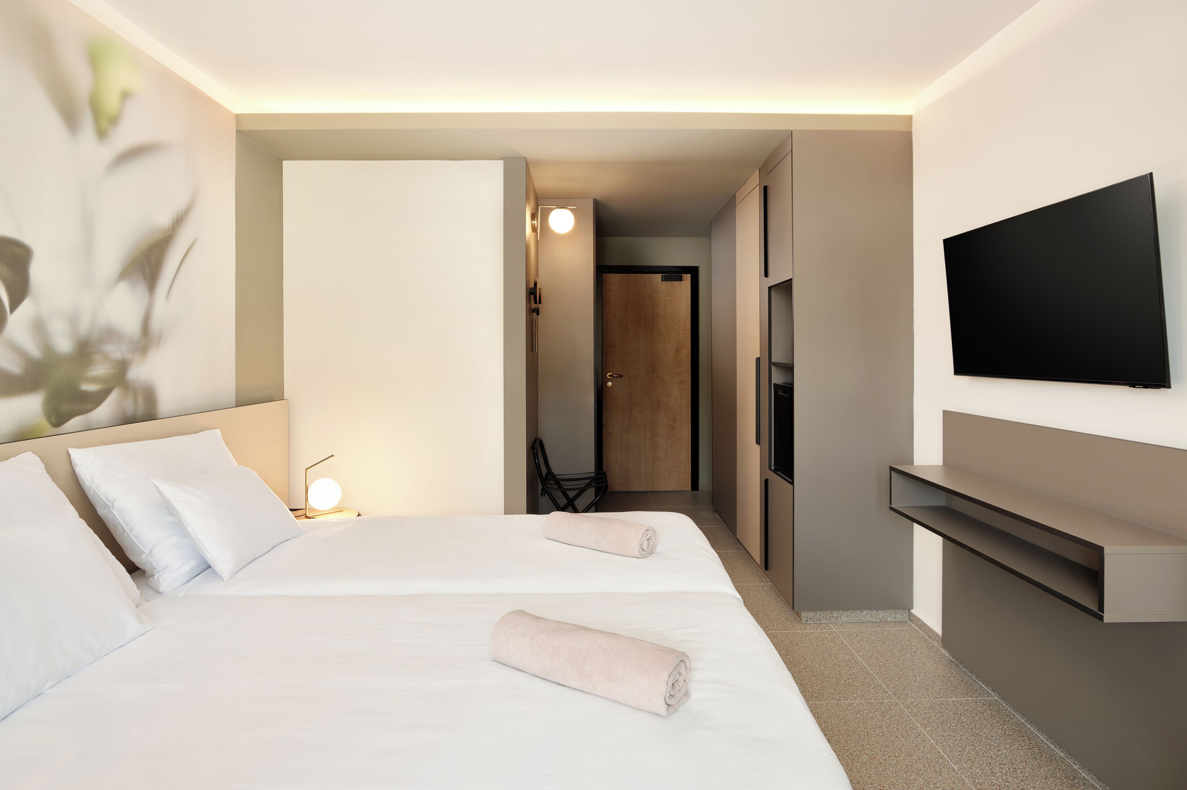 Une chambre d’hôtel avec deux lits, un téléviseur fixé au mur et une petite table avec une lampe.