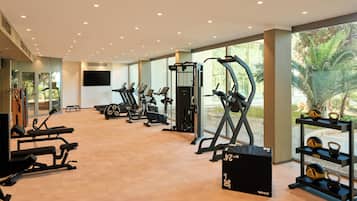 A gym with various exercise equipment, large windows, and a view of greenery outside.