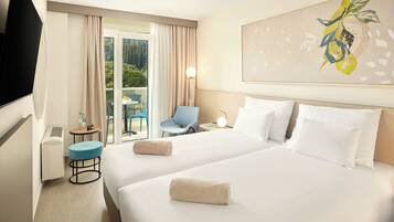 A hotel room with two beds, a TV, a desk with a chair, and a balcony with a table and chairs.