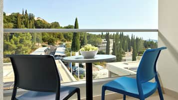 A balcony with two chairs, a table with a bowl of fruit, and a view of a parking area and trees.