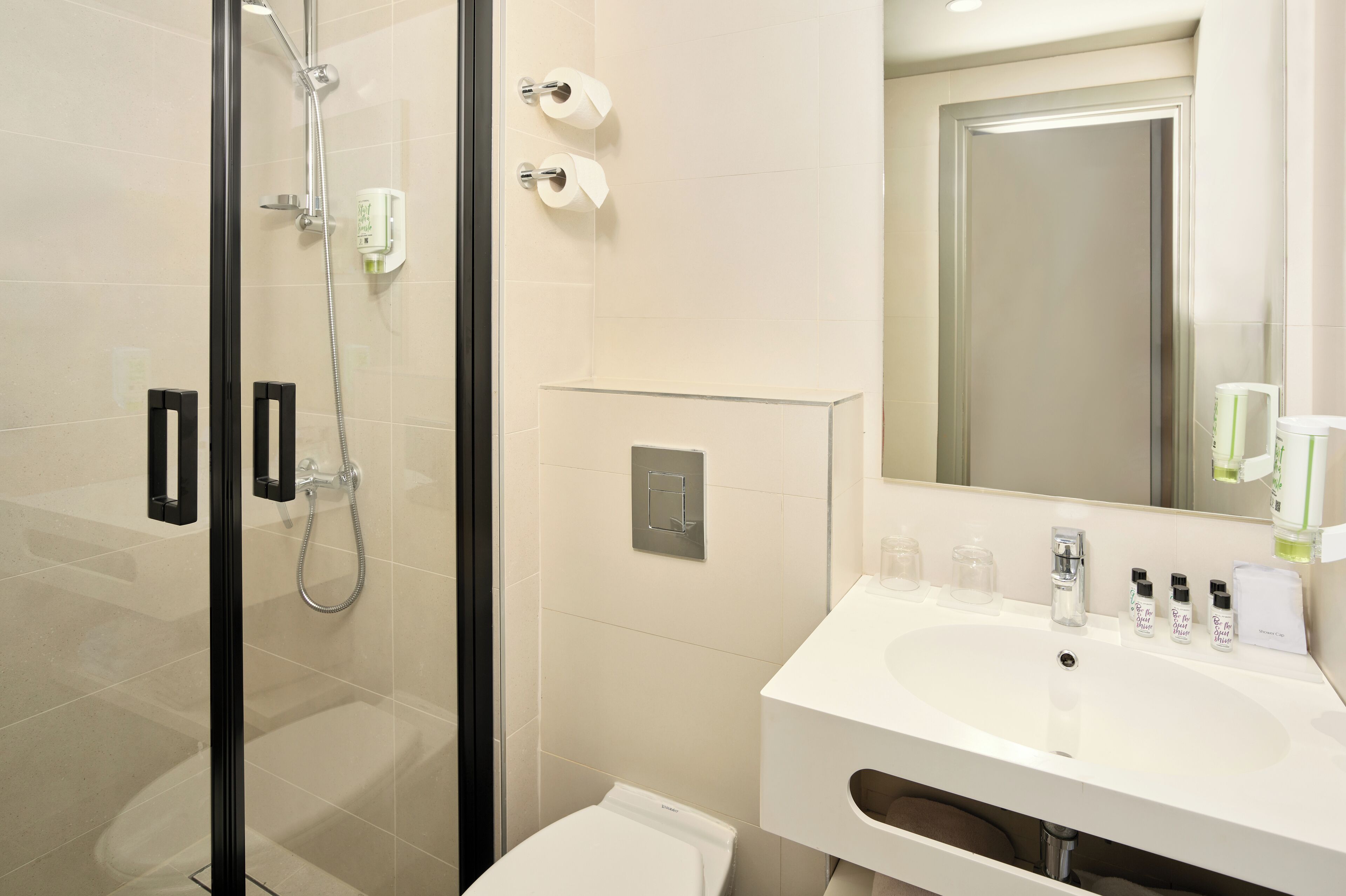 Un baño moderno con cabina de ducha de vidrio, lavamanos blanco con artículos de aseo y un espejo grande.