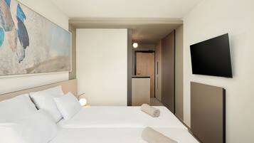 Una habitación de hotel con una cama, un televisor montado en la pared y un cuadro.