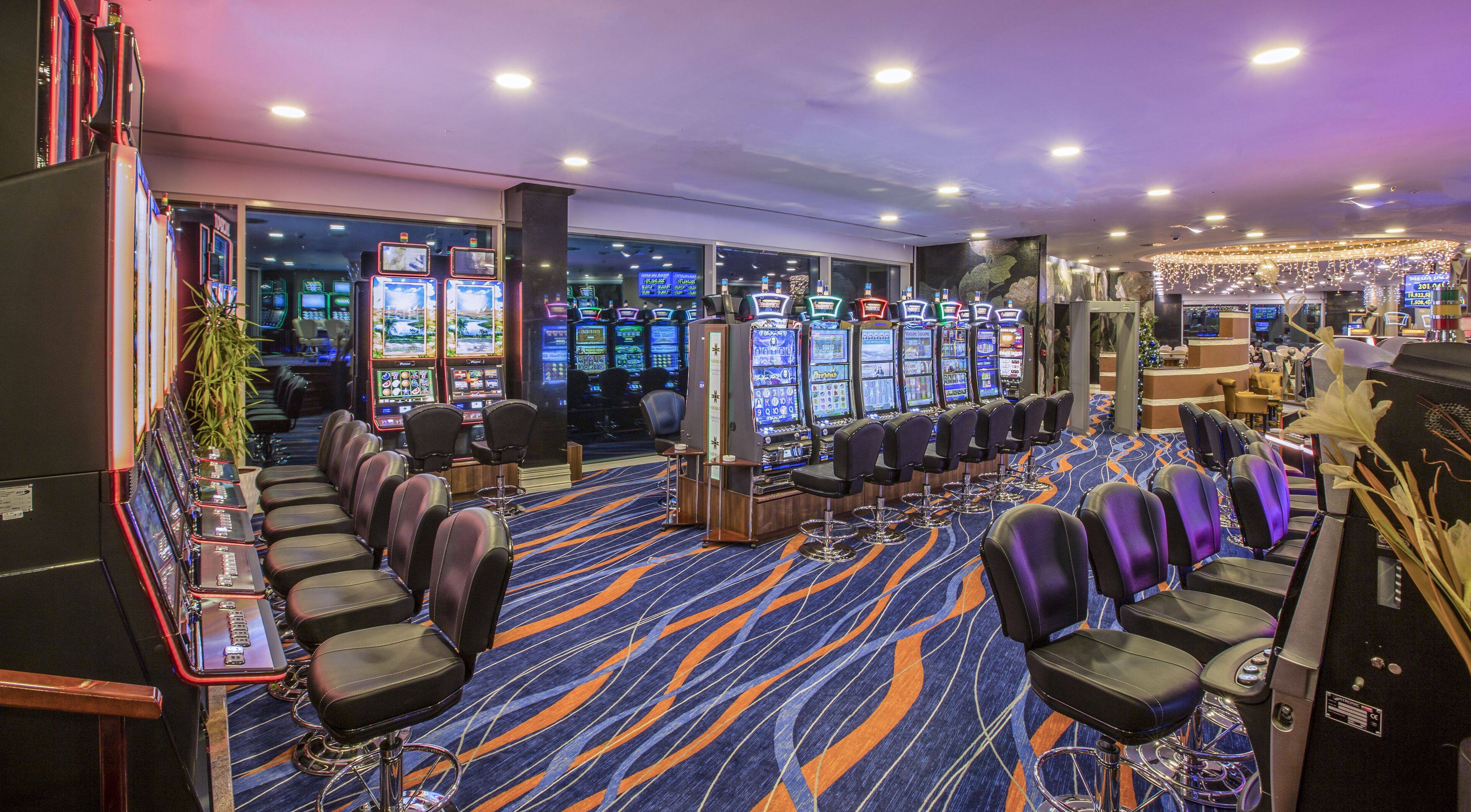 A casino with multiple slot machines, bar seating, and a carpeted floor.