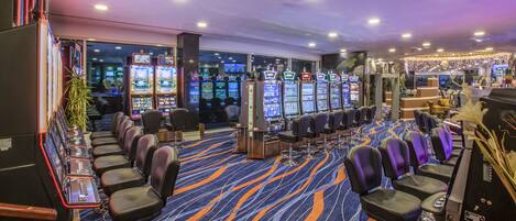 A casino with multiple slot machines, bar seating, and a carpeted floor.