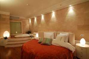 Una habitación de hotel con una cama grande, una bañera y una mesita de noche con lámpara.