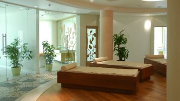 A modern hotel room with a wooden floor, two beds, a large window, and potted plants.