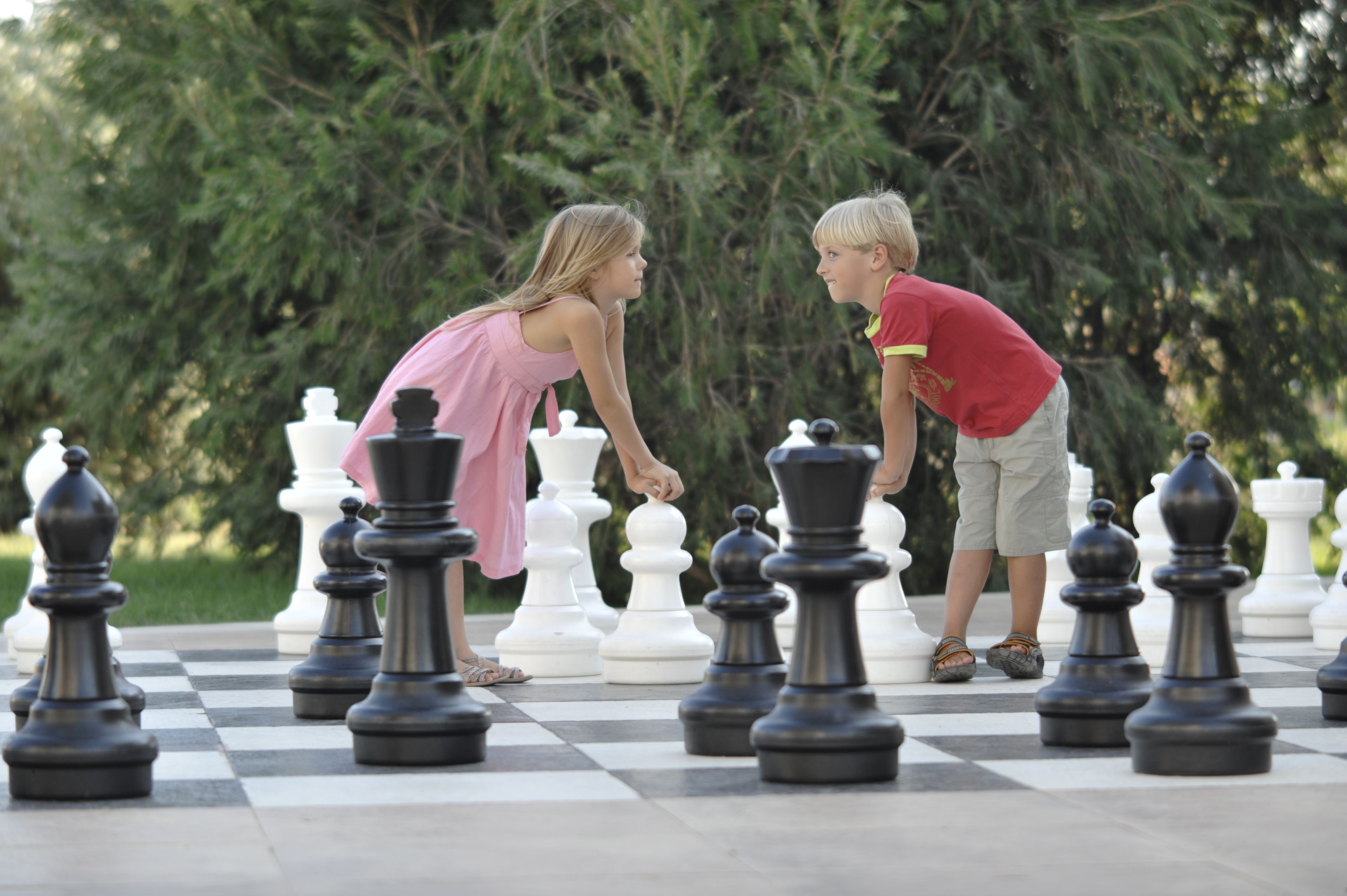 A chessboard with large chess pieces in a park setting.