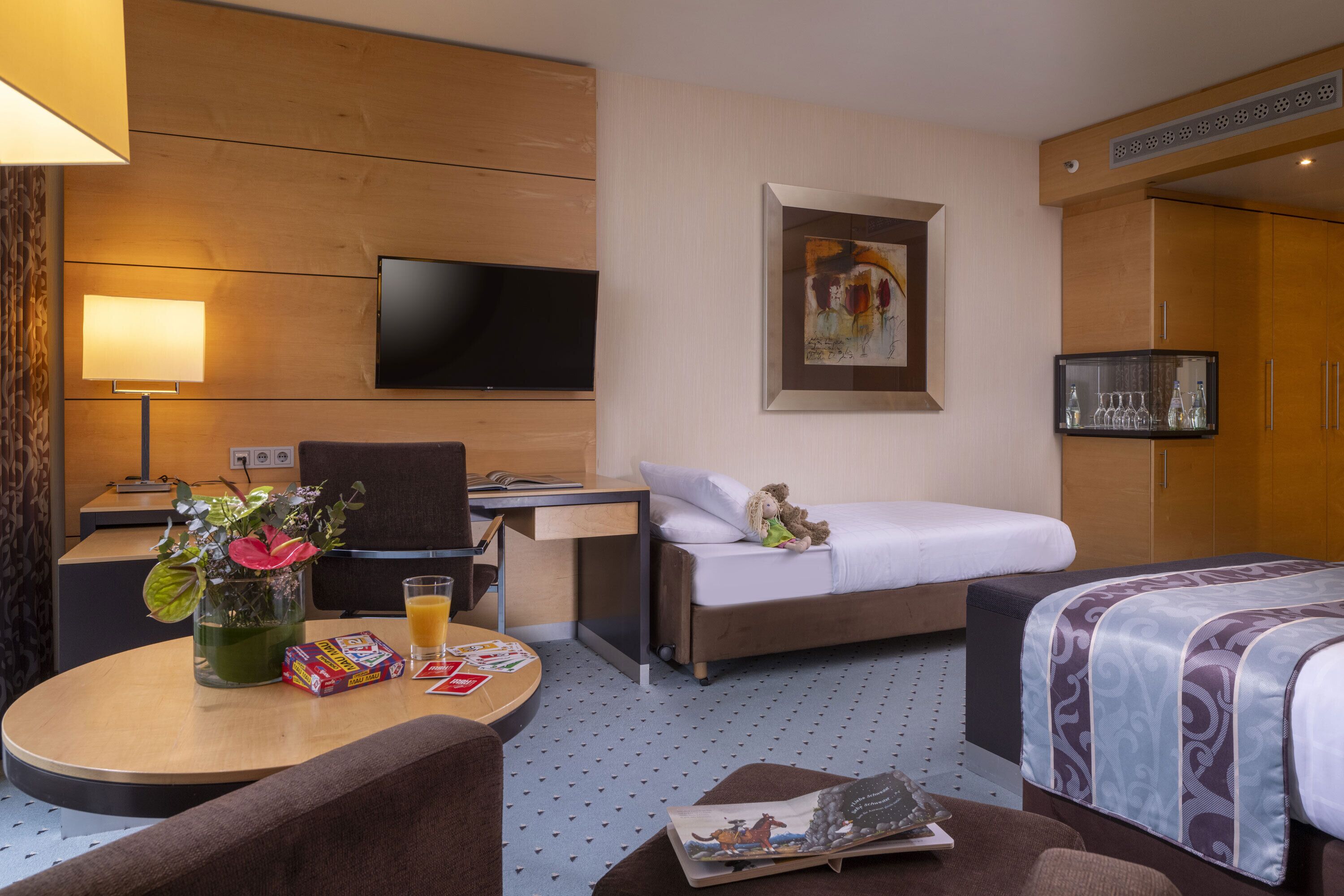 Habitación de hotel con cama, escritorio, televisor, una pequeña mesa con un florero y un sofá.