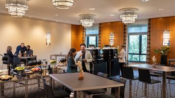 Een restaurantgedeelte van een hotel met meerdere tafels, stoelen en kroonluchters. Gasten dineren en maken er gezellig praatje.