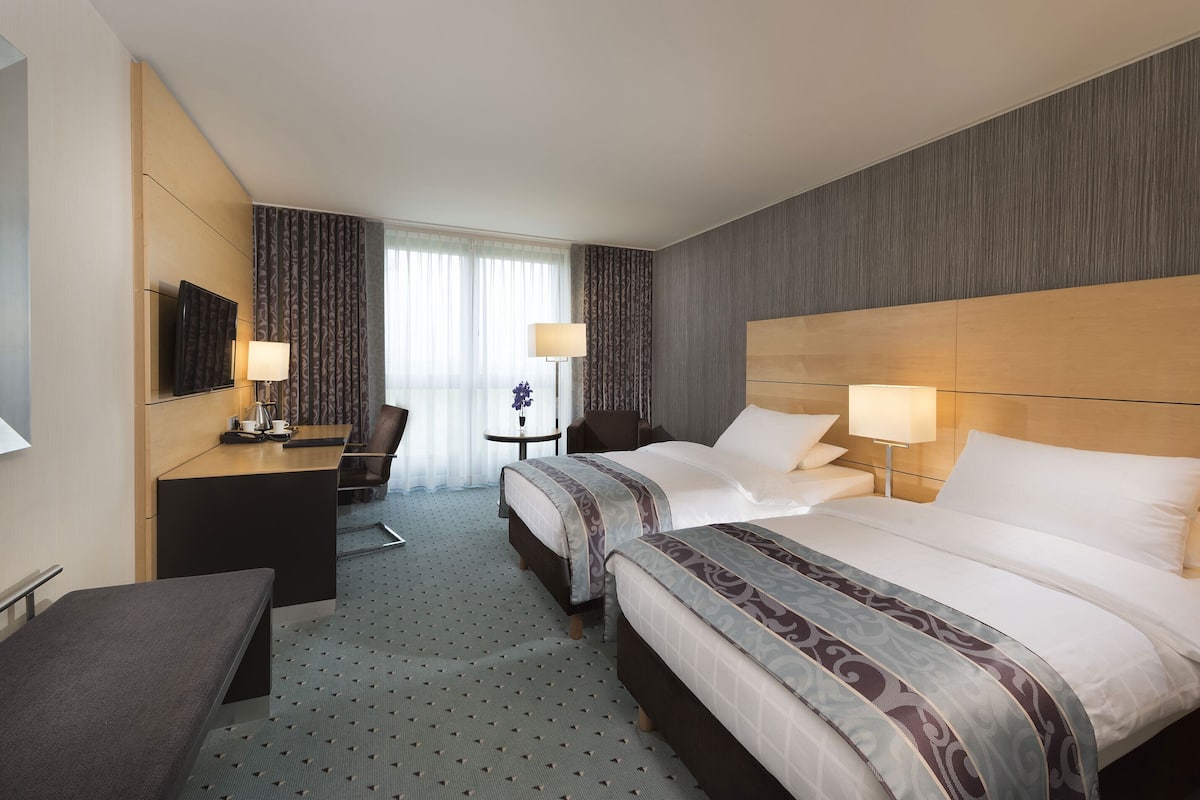 A hotel room with two beds, a desk, a chair, and a TV.