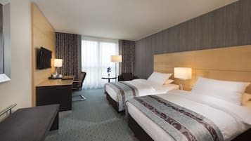 A hotel room with two beds, a desk, a chair, and a TV.