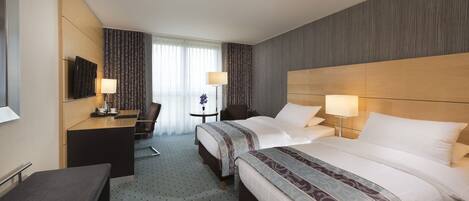 A hotel room with two beds, a desk, a chair, and a TV.