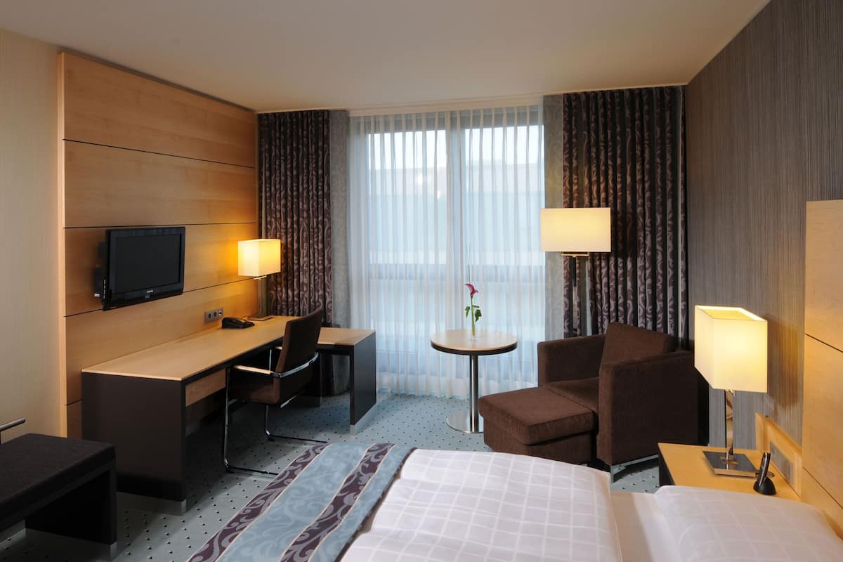 A hotel room with a bed, desk, chair, TV, and two lamps.