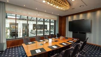 Une salle de conférence équipée d’une grande table, de chaises, d’un téléviseur et de grandes fenêtres.