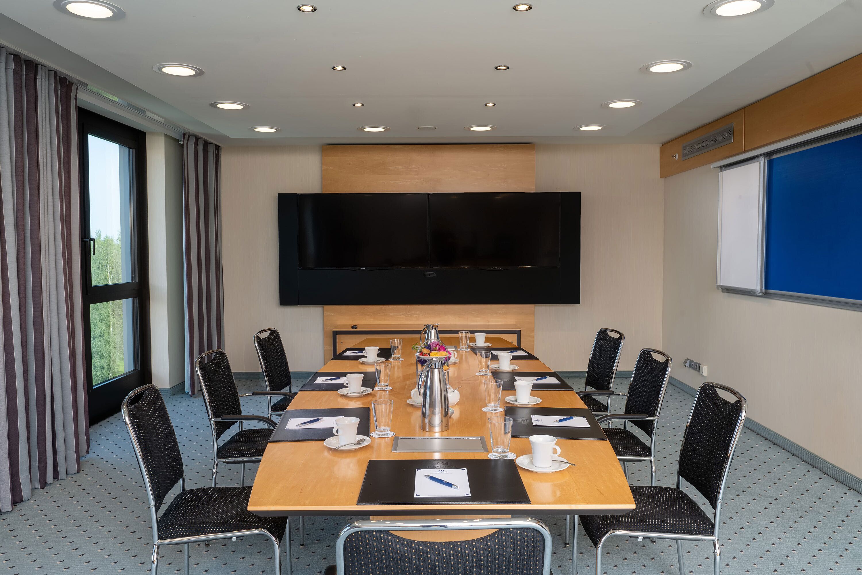 A conference room with a large table, chairs, a flat-screen TV, and a projector screen.